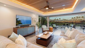 Ein modernes Wohnzimmer mit großem Flachbildfernseher, bequemen Sitzgelegenheiten und Blick aufs Meer.