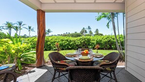 An outdoor patio with wicker chairs and a table set for four, overlooking a lush garden with palm trees. - Hilton Waikoloa pass for 2026. F2 Waikoloa Beach Villas (Waikoloa Beach Resort)