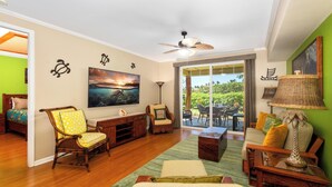 A spacious living room with a large flat-screen TV, wooden furniture, and a view through glass doors to an outdoor area. - Hilton Waikoloa pass for 2026. F2 Waikoloa Beach Villas (Waikoloa Beach Resort)