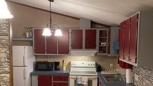 Una cocina compacta equipada con refrigerador, estufa, microondas y pileta. Se observan gabinetes, una encimera y un comedor con mesa y sillas.