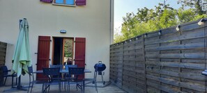 An outdoor patio with a table and chairs, a barbecue grill, and a wooden fence. - Maison Cheptainville Proche Ferme de la Doudou (Cheptainville)