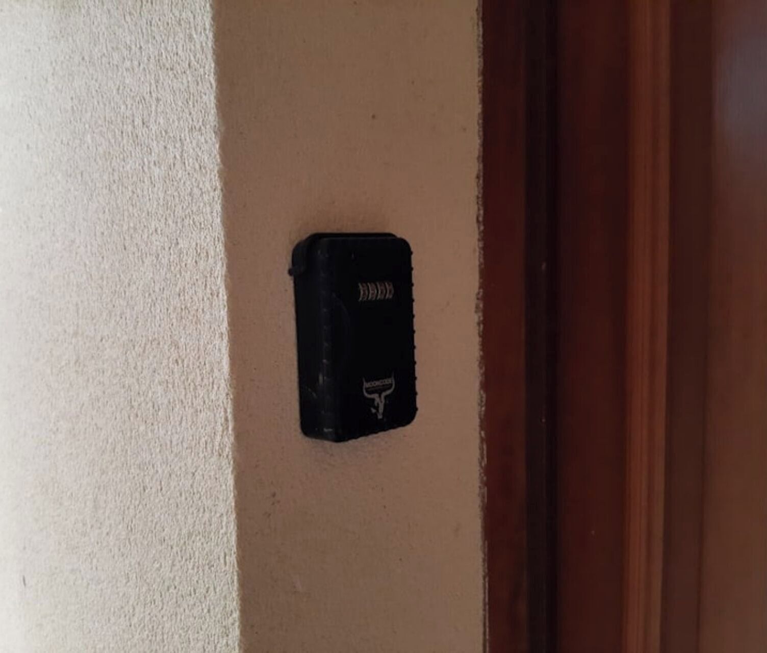 Um objeto preto fixado numa parede bege, possivelmente um dispositivo de segurança ou uma caixa de correio.