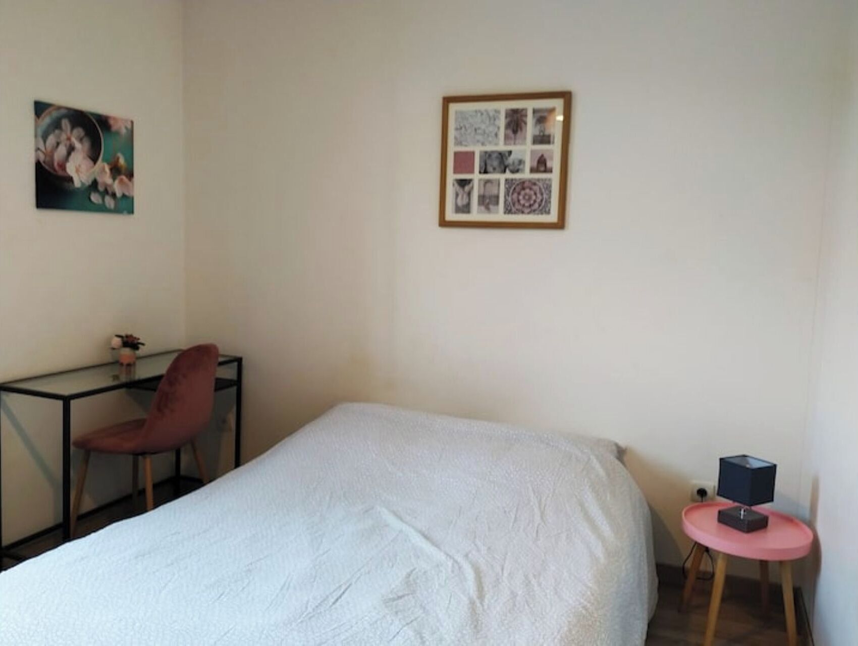 Ein Schlafzimmer mit einem Bett, einem Schreibtisch, einem Stuhl, einem kleinen Tisch mit einem Lautsprecher und einer Wand mit gerahmten Bildern.