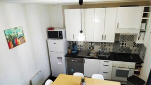 Une cuisine compacte avec des meubles blancs, un four à micro-ondes, un évier et une petite table à manger avec des chaises.