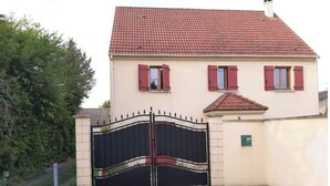 Une maison à deux étages, avec un toit recouvert de tuiles rouges, un portail noir et un mur de couleur beige.
