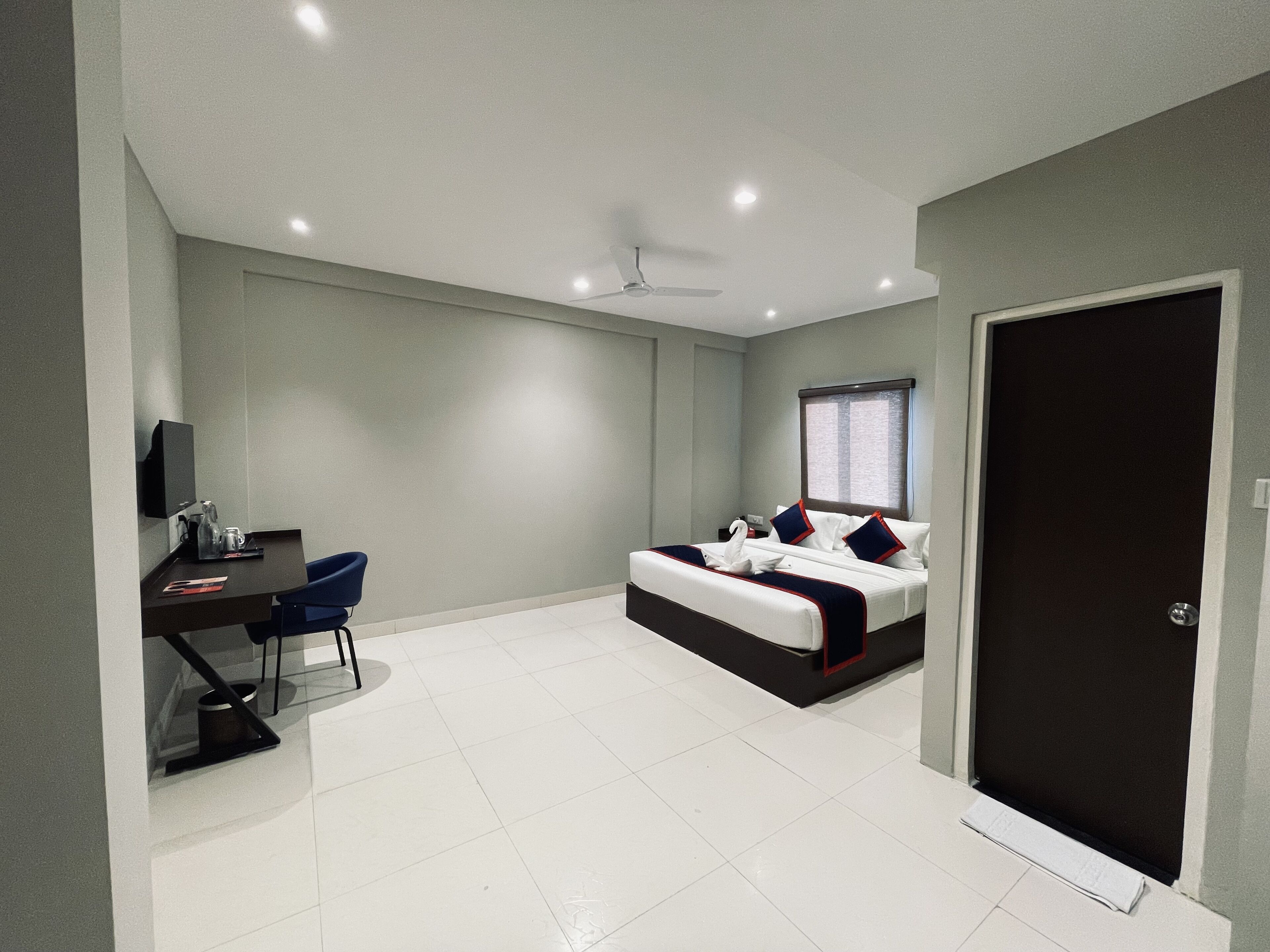 A modern bedroom with a bed, desk, chair, and a door.