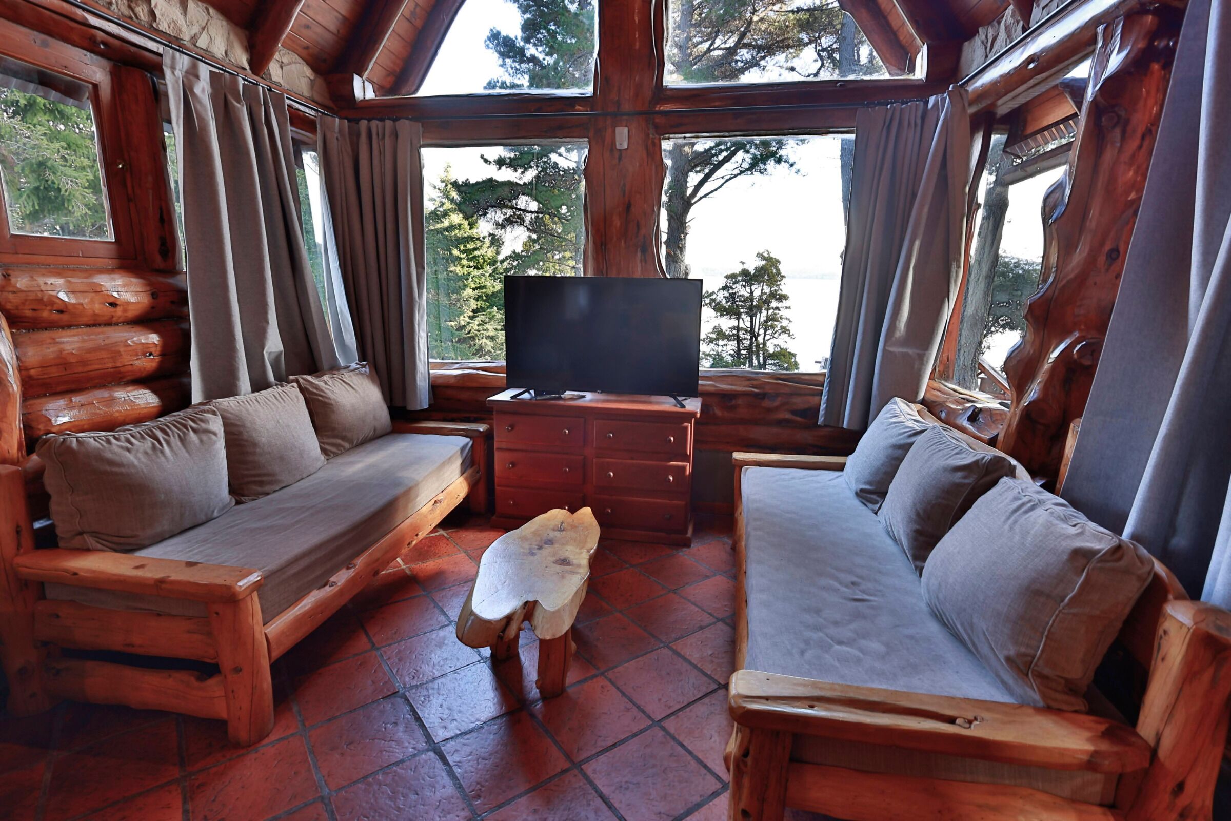 Ein Holzblockhaus-Innenraum mit zwei Holz-Sofas, einem kleinen Tisch und einem Fernseher.