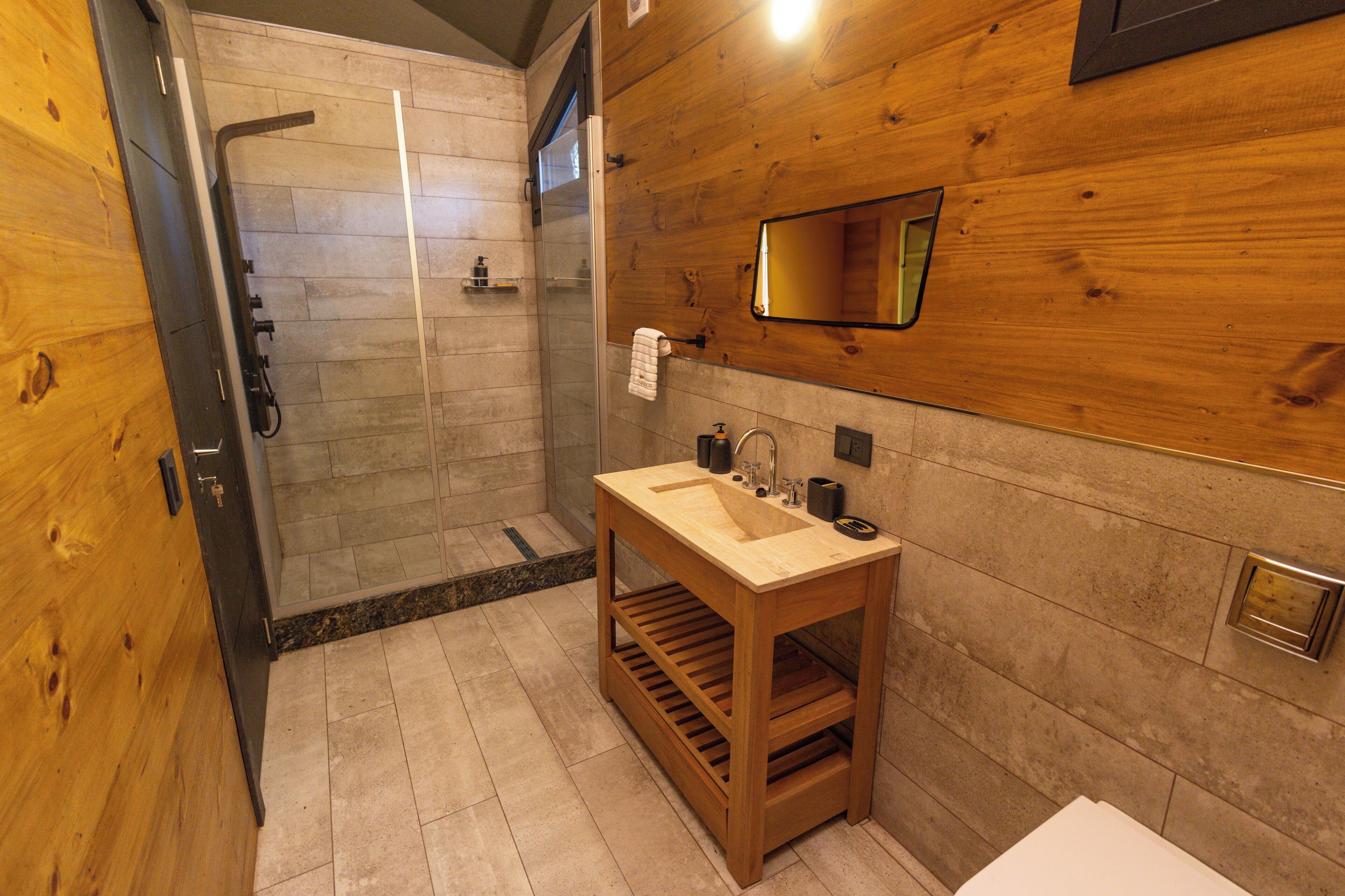 Ein Badezimmer aus Holz mit einer Glasdusche, einem Waschbecken mit Seifenspender und einem Handtuch an der Wand.