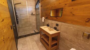 Ein Badezimmer aus Holz mit einer Glasdusche, einem Waschbecken mit Seifenspender und einem Handtuch an der Wand.
