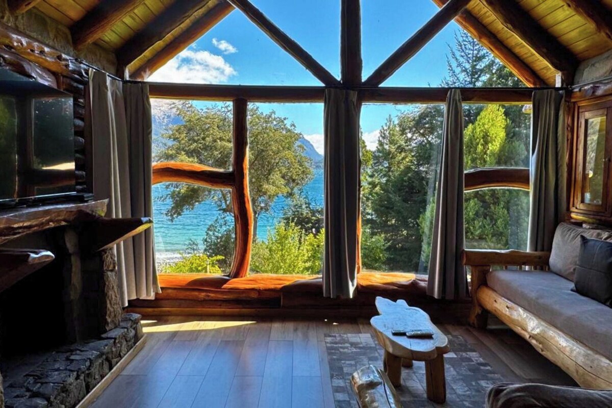 Uma cabana com uma grande janela que oferece vista para um lago e árvores.