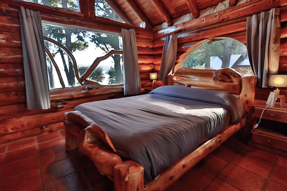 Une chambre dans une cabane en bois, avec un lit, une fenêtre et une lampe.