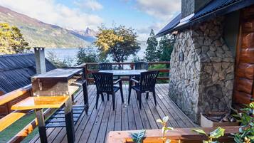 A wooden deck with a stone wall, a table with chairs, and a view of a lake and mountains.