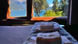 A bed with a view of a lake and mountains through a window. - Villa Labrador Bariloche (San Carlos de Bariloche)