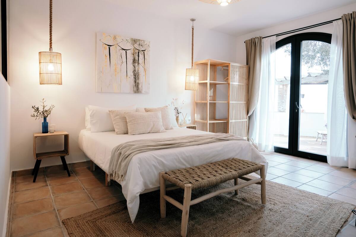 A bedroom with a bed, bedside tables, a bench, and a large window with curtains.