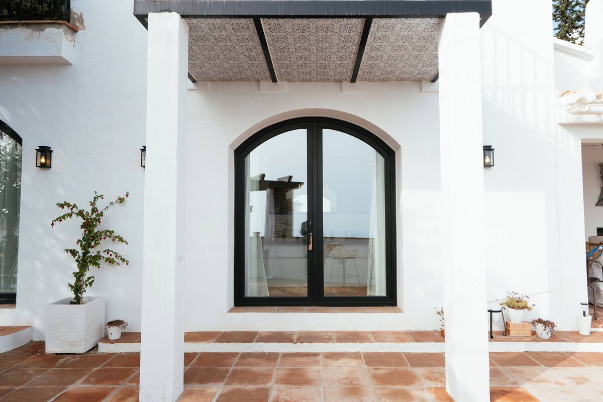 A white building with a large arched glass door, potted plants, and a tiled patio.