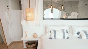 Une chambre à coucher comprenant un lit, une table de chevet, une lampe suspendue, un miroir et une salle de bain visible à travers la porte en verre.