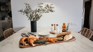 Une table à manger sur laquelle on trouve une variété d’aliments, notamment des croissants, du pain et une plante dans un vase noir.