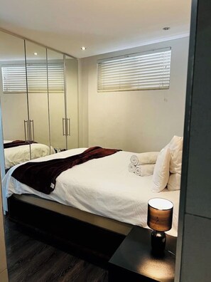 Relax in a serene bedroom with a large bed, bedside table, and mirror.
