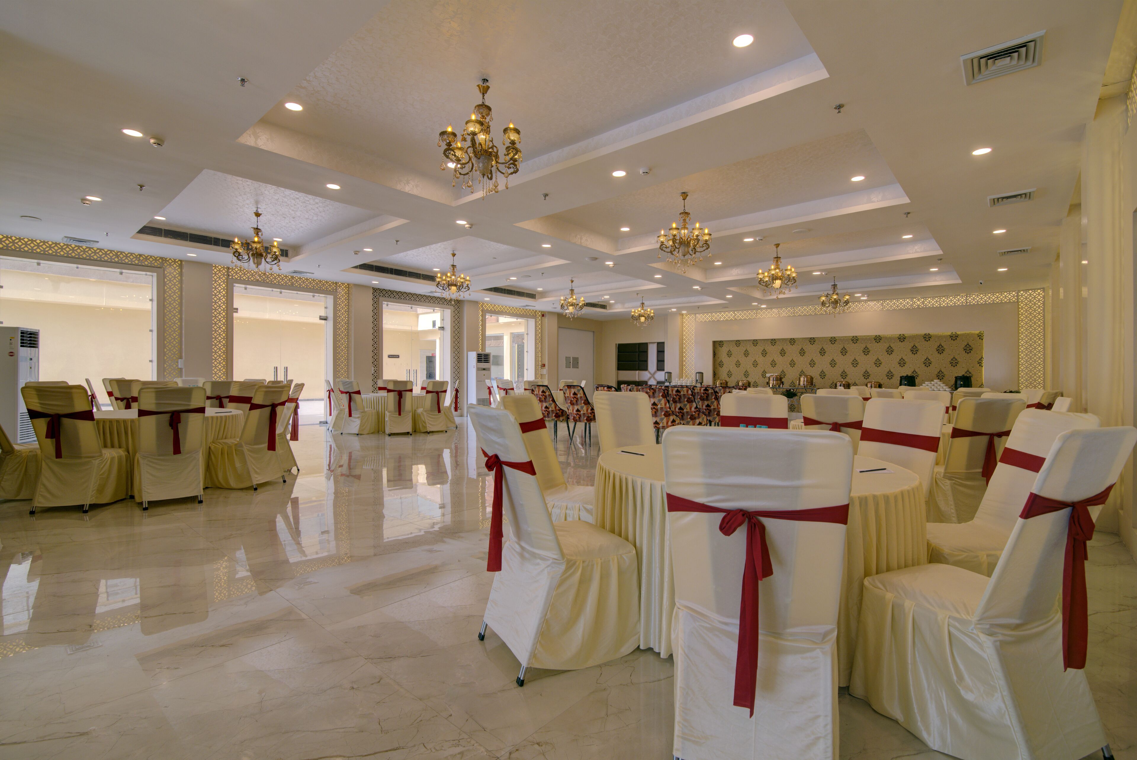 Un salón amplio con filas de sillas adornadas con lazos blancos y rojos, candelabros y un suelo pulido.