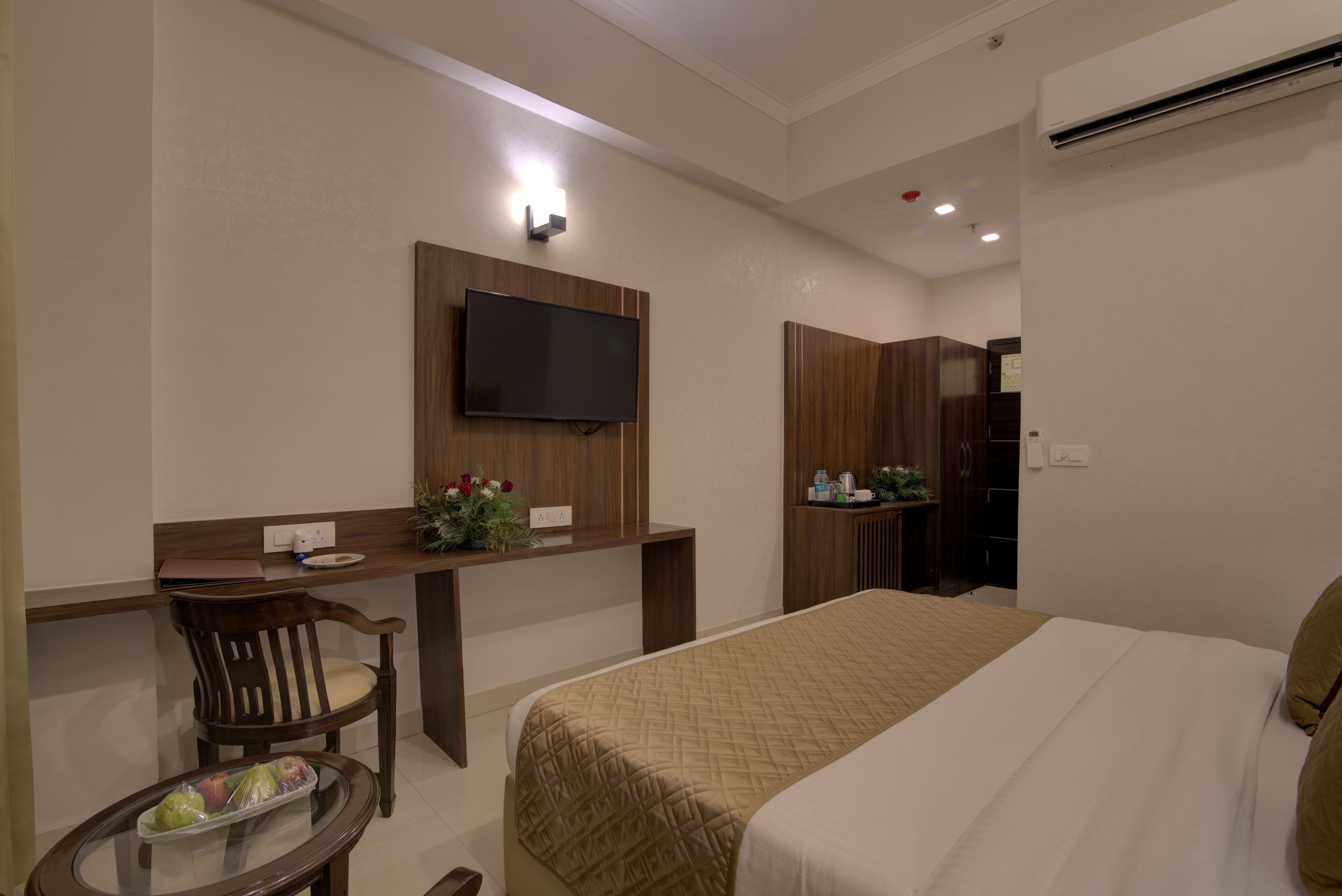 Habitación de hotel con cama, escritorio, silla, televisor y mesita con bandeja de fruta.