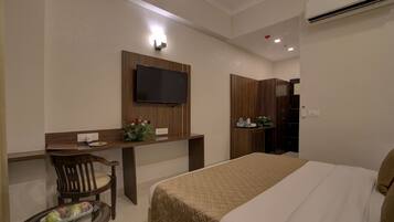 Habitación de hotel con cama, escritorio, silla, televisor y mesita con bandeja de fruta.