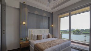 A modern bedroom with a large bed, a nightstand, and a view of a lake through large windows. - Comfort Inn Karnal (Nilokheri)