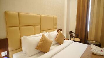A hotel room with a large bed, two pillows, a bedside table, a chair, and a small table with a glass top.