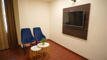 A room with two blue chairs, a small round table with a plant, and a mounted TV on the wall.
