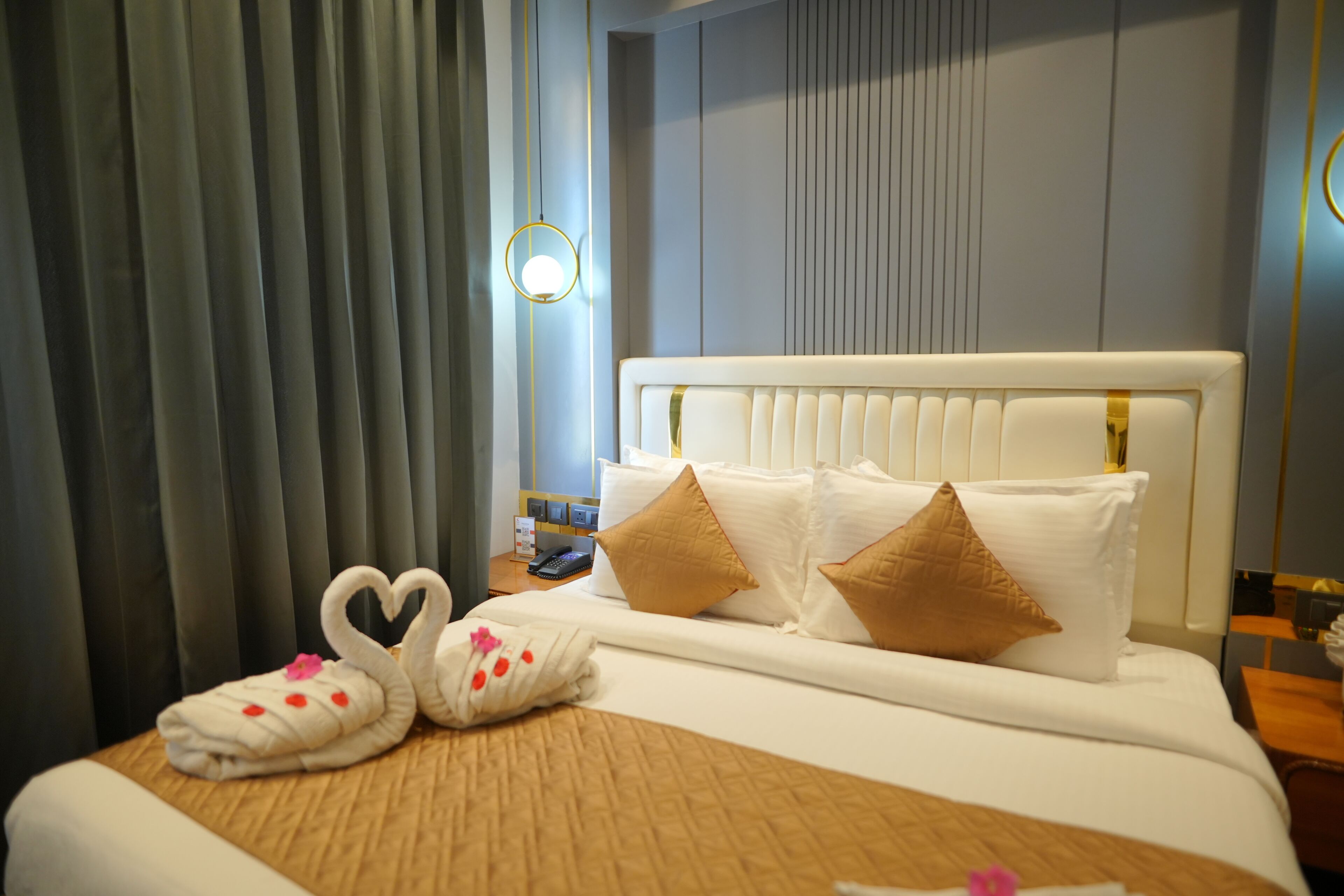 A hotel room with a neatly made bed, a bedside table with a lamp, and a window with curtains.