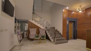A modern interior with a staircase, a seating area with two chairs and small tables, and a wooden wall paneling. - Comfort Inn Karnal (Nilokheri)
