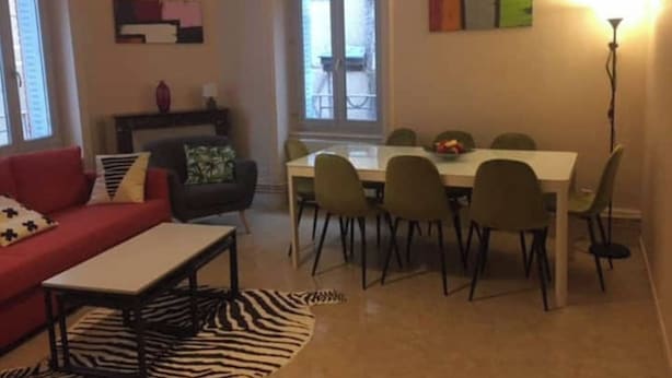 Ett vardagsrum med en röd soffa, en matta med zebrasträck, en matplats med ett vitt bord och stolar samt ett stort fönster.