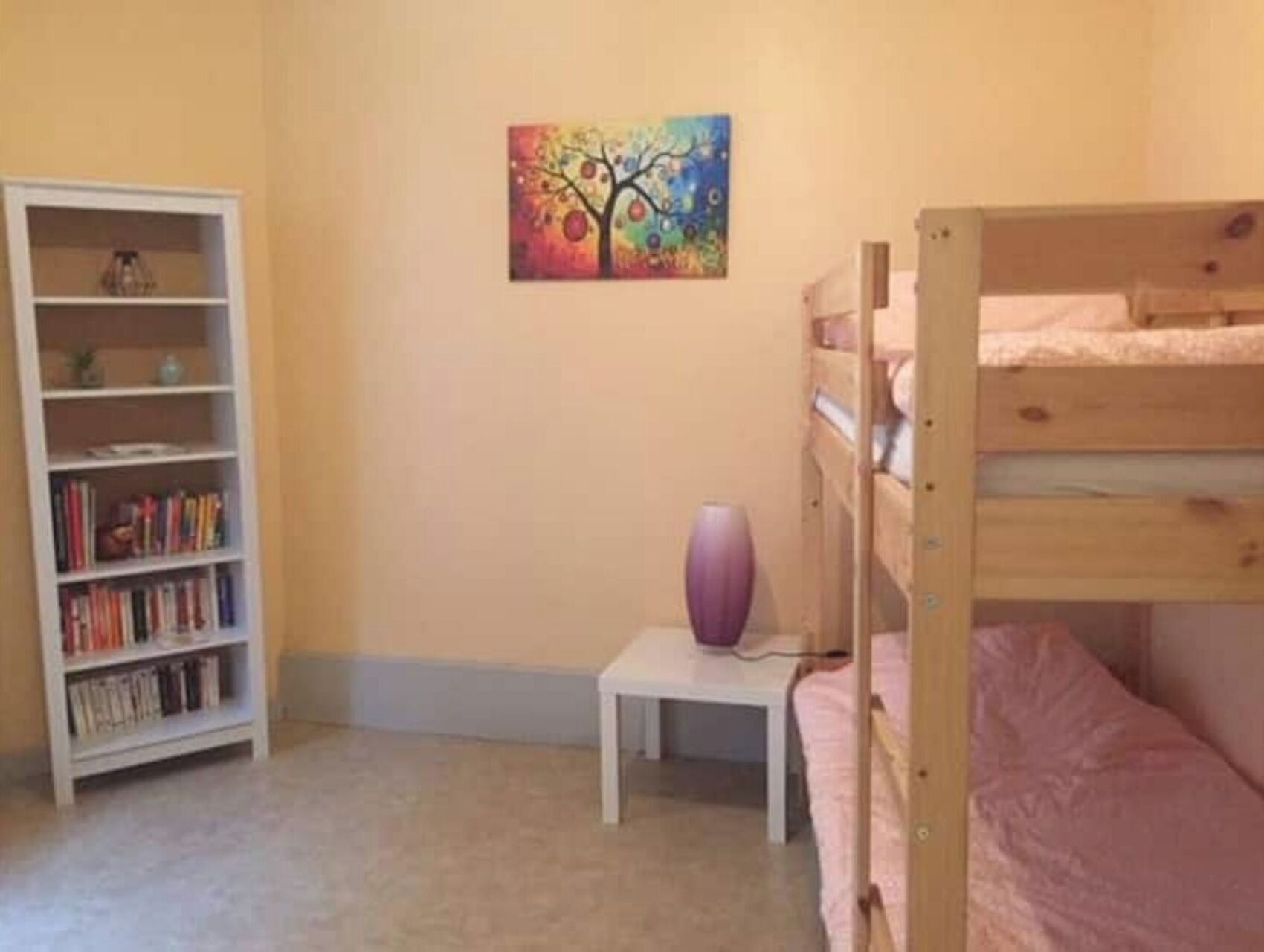 A room with a bunk bed, a bookshelf, and a small table with a vase.