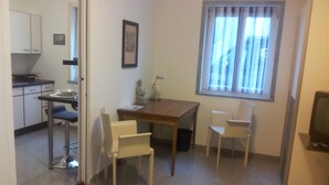 A compact room with a kitchenette, a dining table with four chairs, a small statue, and a window with blinds. - Apartment Graz center (Graz)