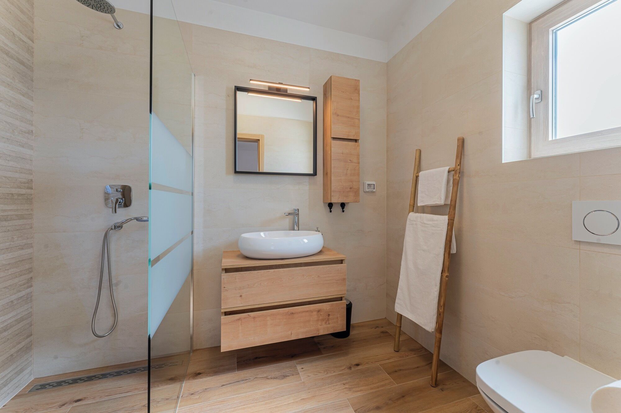 Une salle de bain moderne avec une douche à parois de verre, un lavabo blanc, un meuble-lavabo en bois et un porte-serviettes.