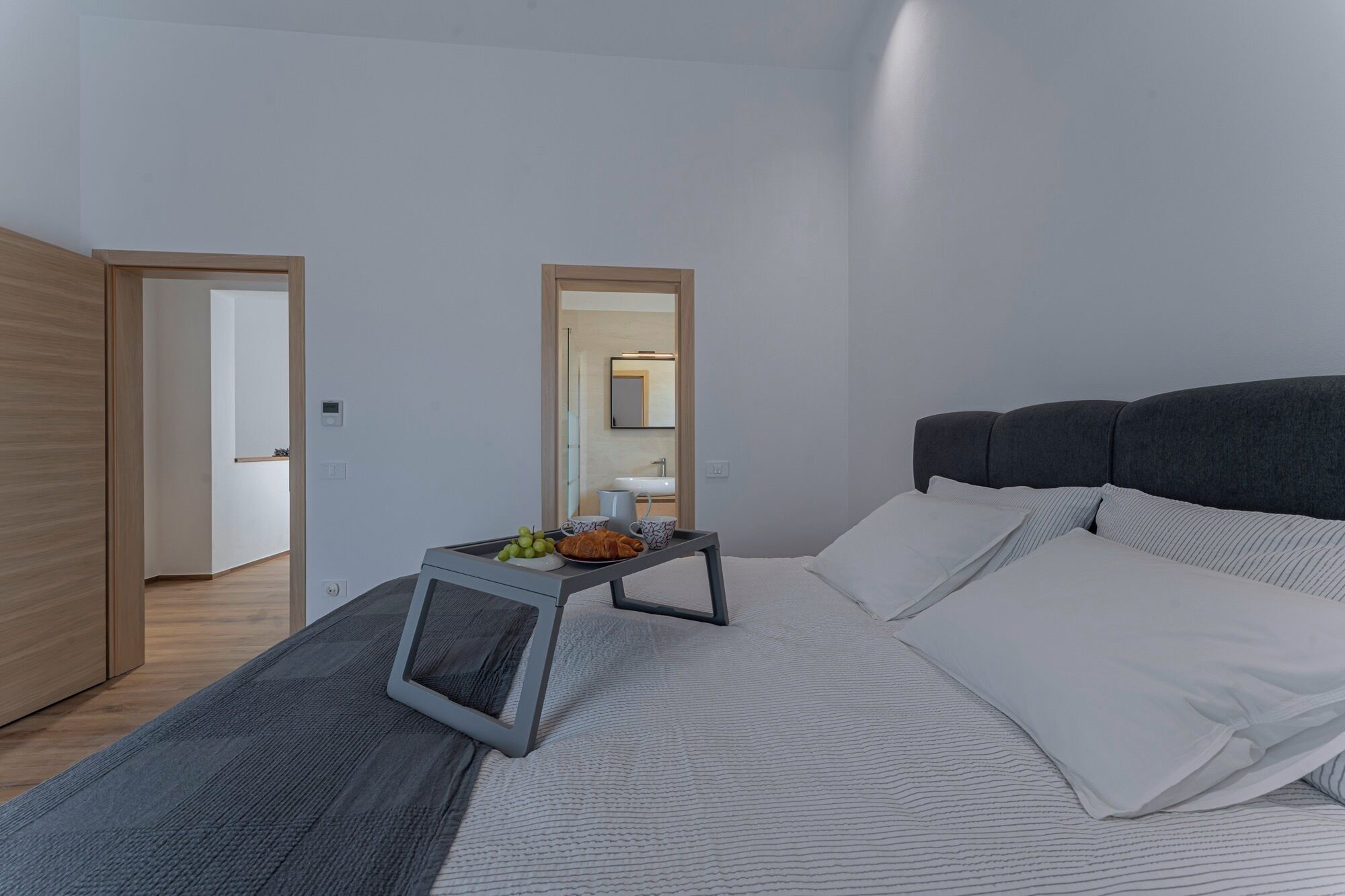 Habitación de hotel moderna con una cama grande, una mesita de noche con espejo y vistas al pasillo.