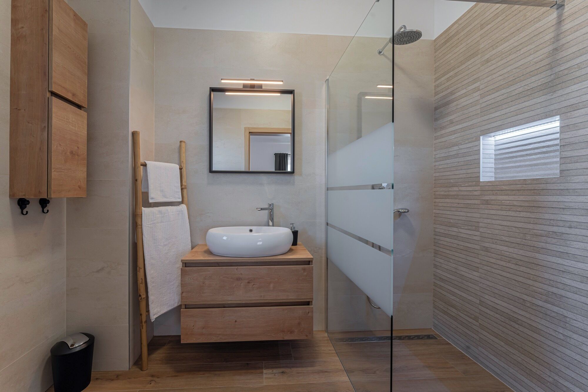 Un baño moderno con tocador de madera, un espejo grande y cabina de ducha de vidrio.