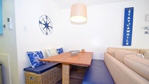 A cozy living area with a wooden table, wicker furniture, a blue sofa, and a wall-mounted sign that reads "STAY WHILE".