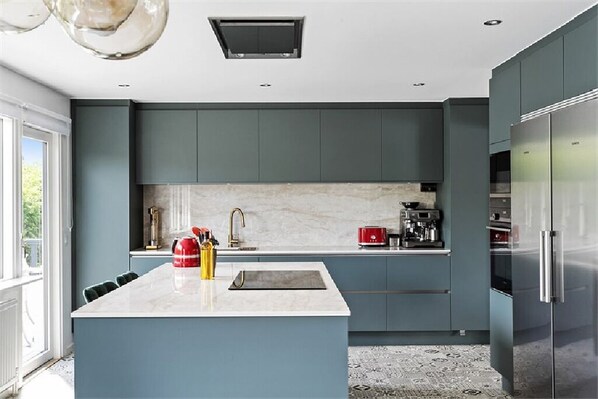 A modern kitchen with a central island, dark cabinetry, and stainless steel appliances. - Vistelse House (Hallands län)