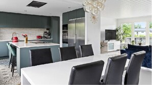 Une cuisine moderne dotée d’un îlot central, de meubles de couleur sombre et d’un coin repas avec une table blanche et des chaises noires.