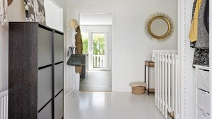 Un couloir avec un sol blanc, un radiateur, un miroir et une porte donnant sur un balcon.