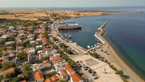 An aerial view of a coastal town with a prominent ferry dock, a marina with boats, and a mix of residential buildings with red-tiled roofs.