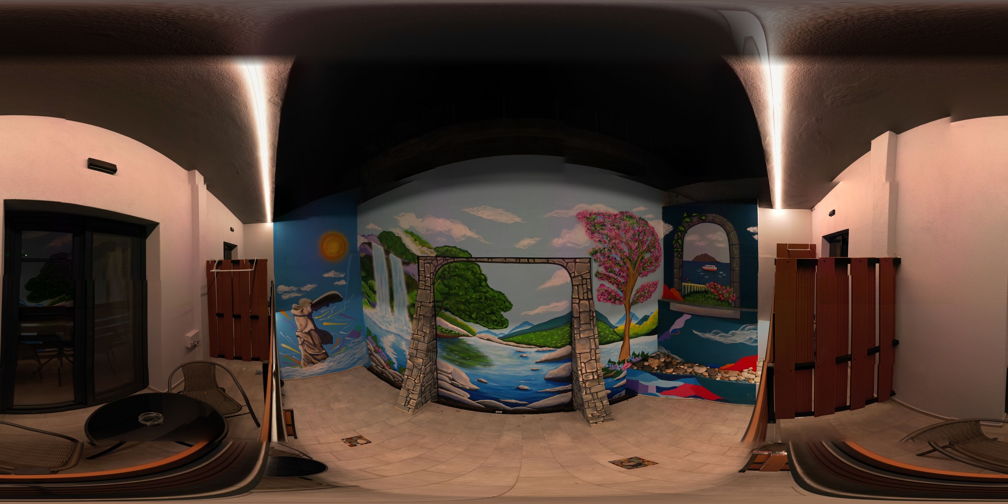 Una habitación con un mural de un paisaje, un arco de piedra y vistas al exterior a través de un ventanal.