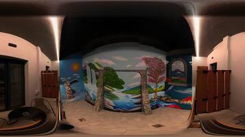 Una habitación con un mural de un paisaje, un arco de piedra y vistas al exterior a través de un ventanal.