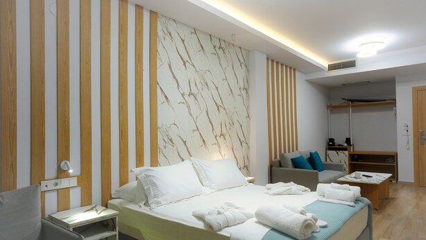 A modern hotel room with a bed, bedside tables, a sofa, and a walk-in closet.