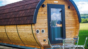 Una cabaña de madera con techo curvo, una puerta y una pequeña mesa con sillas afuera.