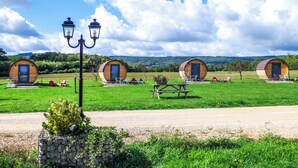 Tres cabañas de madera redondas con puertas, una mesa de picnic y un farol en un campo cubierto de césped.