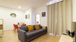 Un salon moderne avec un canapé gris, des fauteuils rouges, un bureau en bois et une grande fenêtre avec des rideaux.