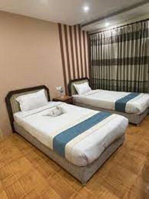 A hotel room with two single beds, wooden flooring, a window with curtains, and a nightstand with a lamp. - Centrally located at west Thamel quite Location 5 stories Apartment  (Kathmandu)