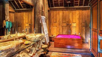 A rustic wooden bathroom with a large bathtub, stone sinks, and a mirror.