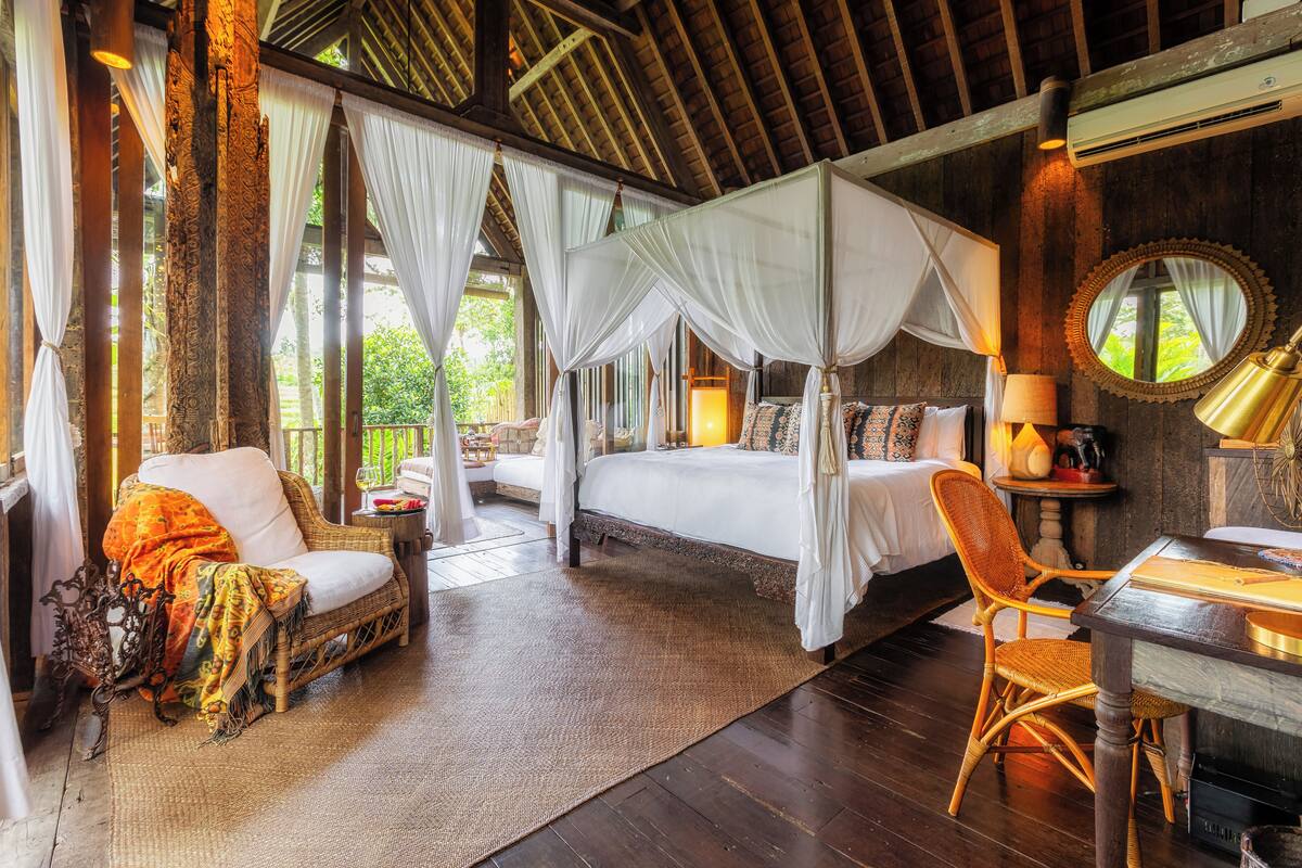 A spacious room with a large bed, a sitting area with a chair and table, and a view of the outdoors.